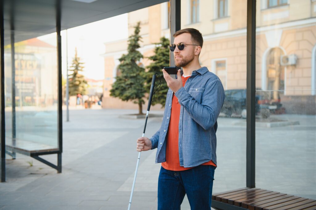 Niewidomy mężczyzna z telefonem komórkowym czekający na autobus na dworcu autobusowym.
